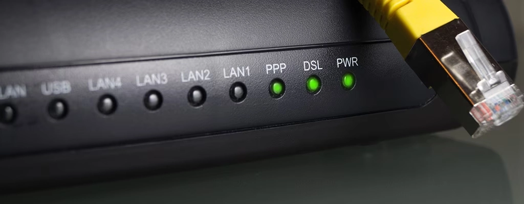 Painel frontal de modem com luzes indicadoras DSL, PPP e LAN acesas e cabo de rede conectado, ilustrando a diferença entre modem e roteador na conexão com a internet.
