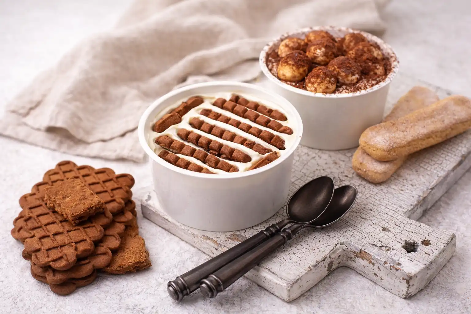 Cheesecake japonês em comparação com versão viral feita com iogurte e biscoito, mostrando sobremesas cremosas em potes brancos com camadas de biscoito speculoos e cacau, destacando a diferença entre a receita original e a adaptação popular das redes sociais.