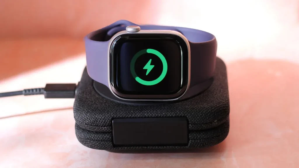 Apple Watch carregando na base magnética, com indicador de bateria na tela, ilustrando a diferença entre Apple Watch Series 11 vs. Series 10 em autonomia e carregamento rápido.