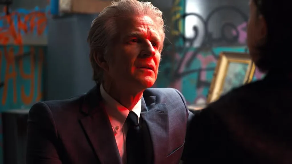 Dr. Brenner em Stranger Things aparece em uma cena tensa, usando terno e com expressão séria sob iluminação avermelhada, representando o cientista manipulador e destacando a diferença entre Dr. Brenner e Dr. Kay em Stranger Things.