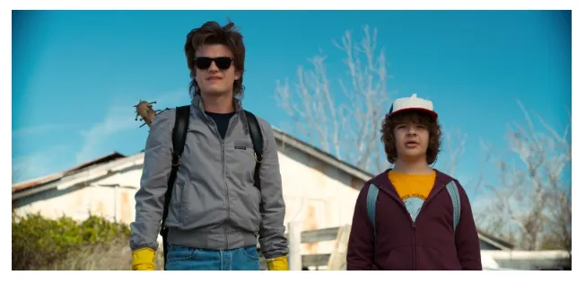 Cena da série Stranger Things com Steve Harrington e Dustin Henderson caminhando juntos em Hawkins, destacando a amizade entre os personagens e o tom aventureiro da série em contraste com Dark, na comparação Dark vs Stranger Things.