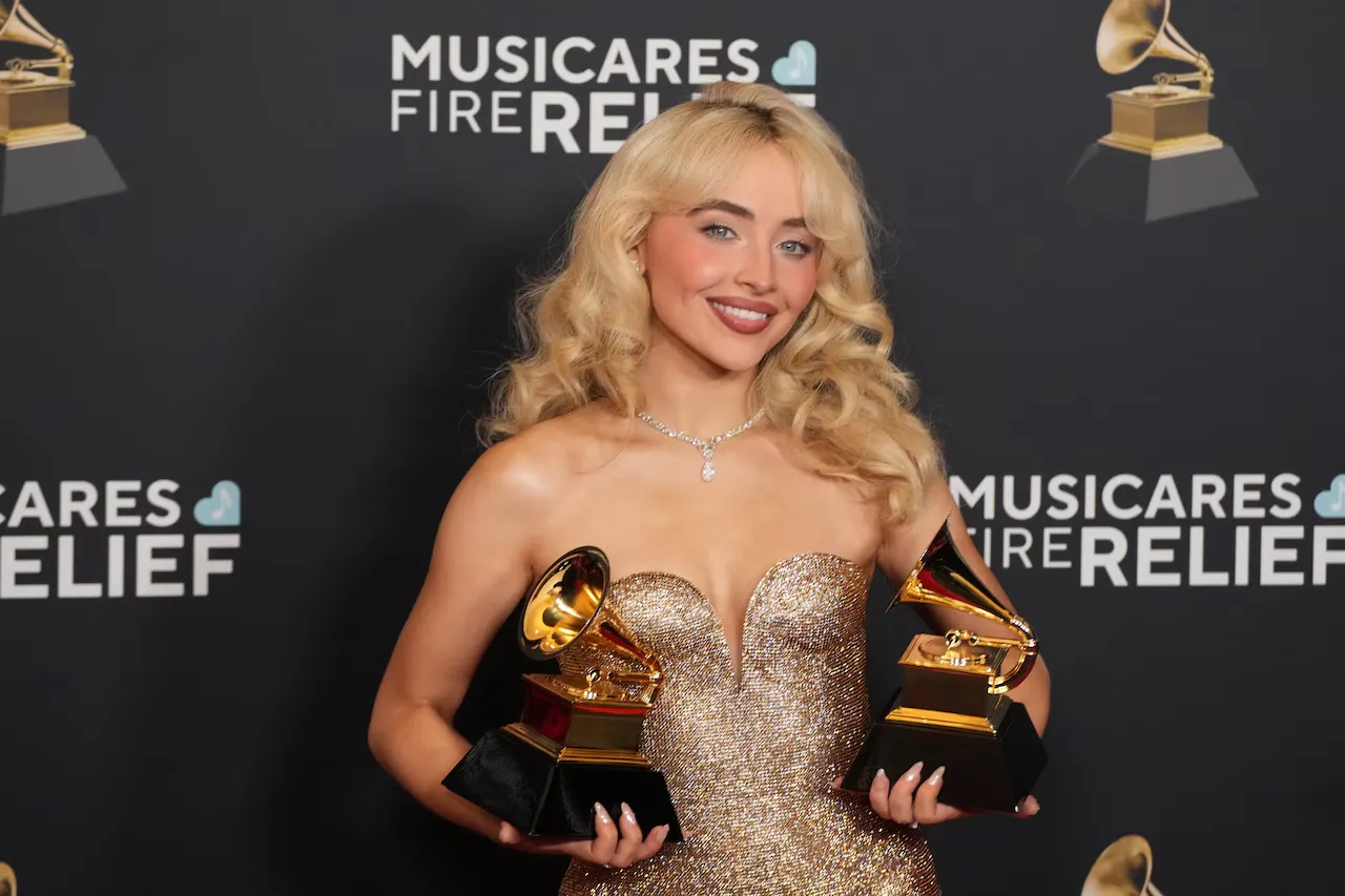Artista segurando dois troféus do Grammy Awards em evento oficial, representando as principais categorias do prêmio e ilustrando a diferença entre Canção do Ano e Gravação do Ano no Grammy.