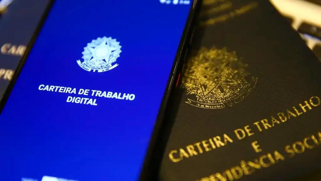 Carteira de Trabalho Digital exibida na tela de um celular ao lado da Carteira de Trabalho física, ilustrando consulta de dados trabalhistas e acesso a benefícios como PIS e PASEP.