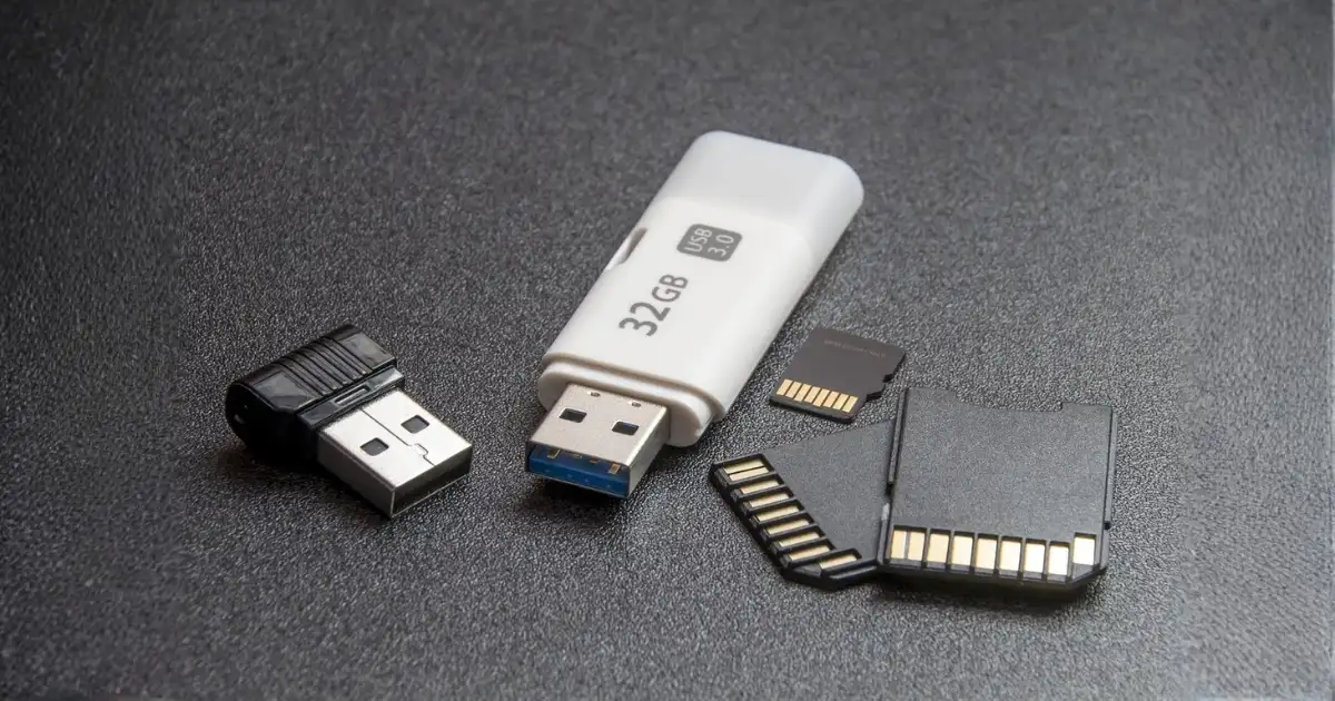 Pendrive USB 3.0 de 32GB ao lado de adaptador USB e cartões de memória SD e microSD sobre superfície escura, ilustrando dispositivos de armazenamento usados para transferência de arquivos e procedimentos de como formatar pendrive.