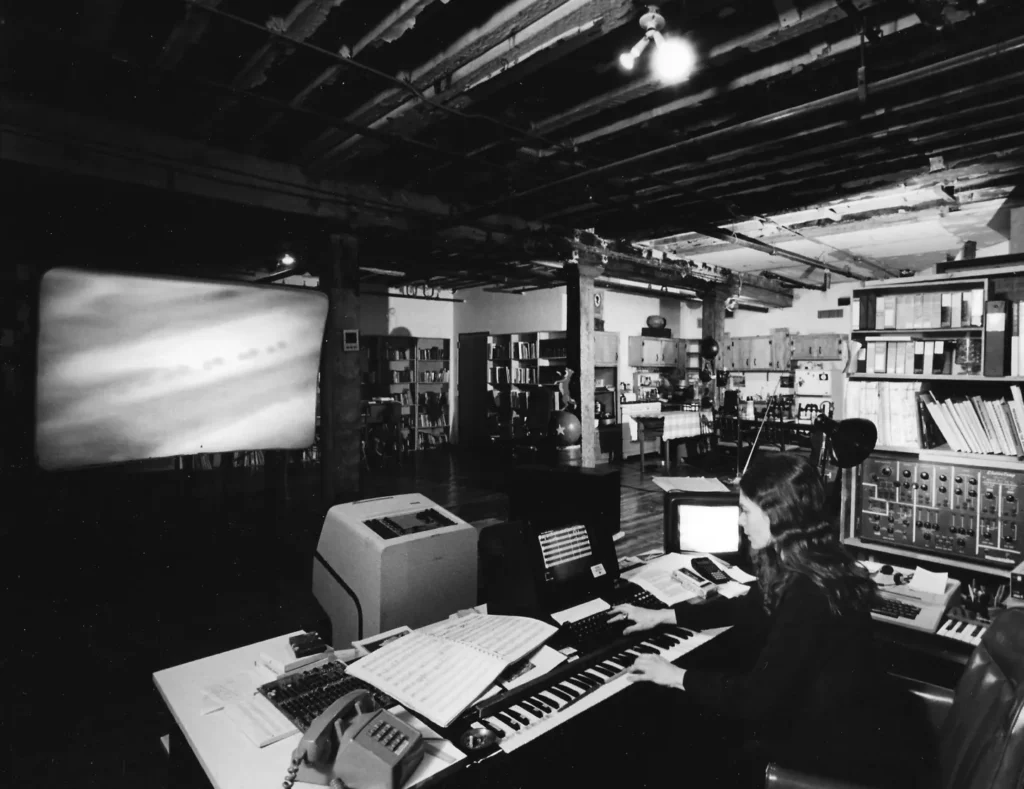 Laurie Spiegel trabalhando em estúdio experimental nos anos 1985 com sintetizadores e computador no Bell Labs, imagem histórica relacionada à diferença entre música algorítmica e IA.
