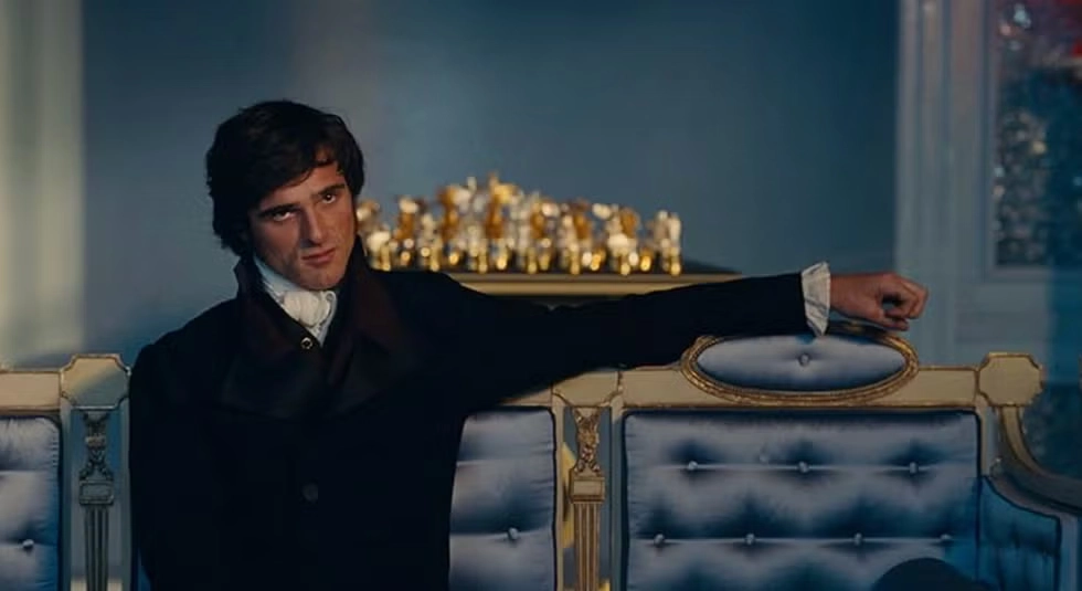 Heathcliff no filme O Morro dos Ventos Uivantes (Wuthering Heights), sentado em um sofá elegante em ambiente aristocrático, destacando a diferença entre o livro O Morro dos Ventos Uivantes e o filme na adaptação cinematográfica.