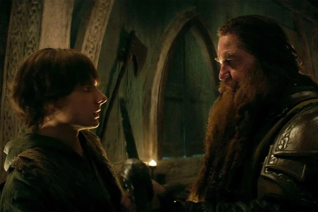 Cena da versão live-action de Como Treinar Seu Dragão mostrando Soluço conversando com Stoico em ambiente iluminado por tochas, destacando as diferenças emocionais entre a adaptação em live-action e a animação original. Crédito: Universal Pictures