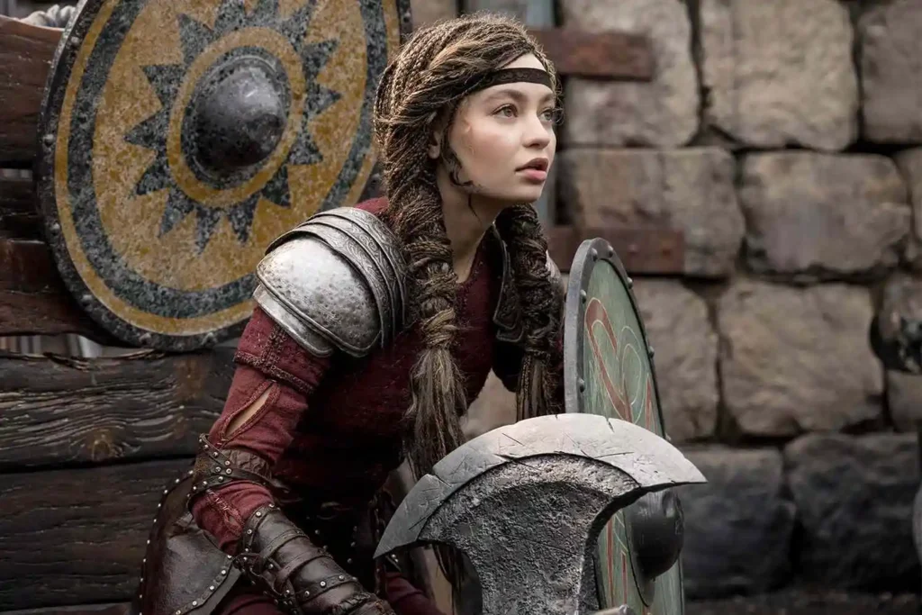 Astrid na versão live-action de Como Treinar Seu Dragão segurando escudo e machado em cenário viking, destacando as diferenças visuais e o realismo da adaptação em comparação com a animação original. Crédito: Universal Pictures