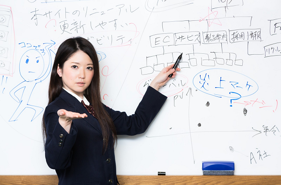 Estudante japonesa do ensino médio apresentando conteúdo no quadro branco em sala de aula — imagem que ilustra liderança escolar e reforça como o ensino médio nos animes é diferente do ensino médio real.