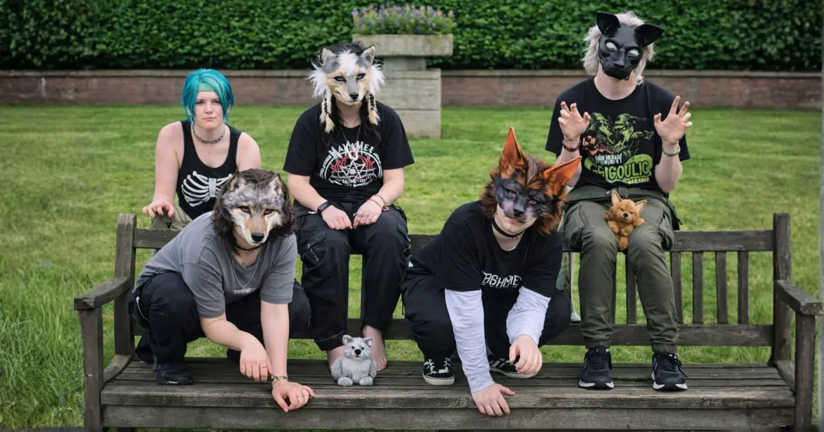 Grupo de jovens usando máscaras de animais e roupas escuras sentados e agachados em um banco de parque, representando a estética associada ao tema “O que são therians e em que eles diferem dos furries” e às diferenças entre furries e therians.