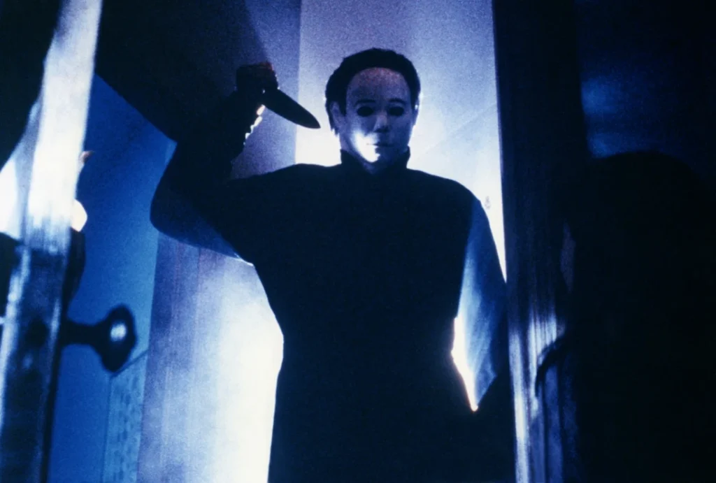 Cena escura de filme de horror com figura mascarada segurando uma faca, representando o medo e a ameaça constantes usados para explicar qual a diferença entre horror e suspense