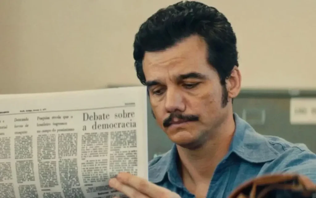 Cena do filme O Agente Secreto, indicado ao Oscar 2026, mostrando personagem lendo jornal em momento dramático, representando o ranking dos 10 filmes do Oscar 2026.